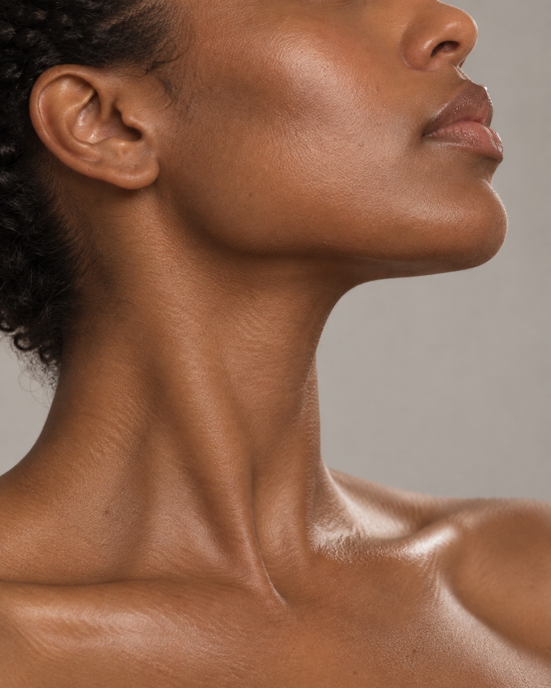 A jawline in profile against a plain greige ground, chin slightly raised